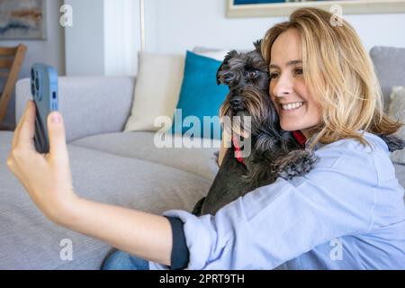 Jeune belle femme ayant beaucoup de temps avec son petit chien doux à la maison, prenant beaucoup de photos. Concept de style de vie et d'amitié. Banque D'Images