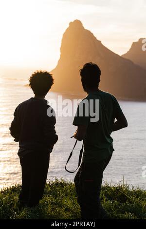 Découvrez la beauté des natures. Vue arrière de deux hommes jouissant d'une vue sur l'océan depuis une colline. Banque D'Images