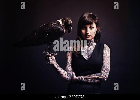 Femme fatale. Photo studio d'une jeune femme tatouée tenant un oiseau Banque D'Images