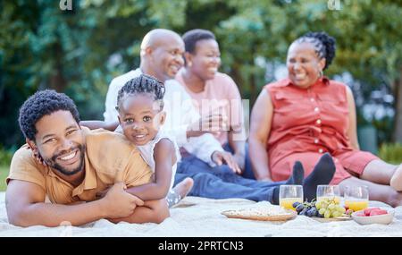 Portrait d'un père et d'un enfant noirs lors d'un pique-nique en famille dans un jardin vert extérieur au printemps. Souriez, heureux et africains manger des fruits sains lors d'une fête à l'extérieur dans un parc. Banque D'Images