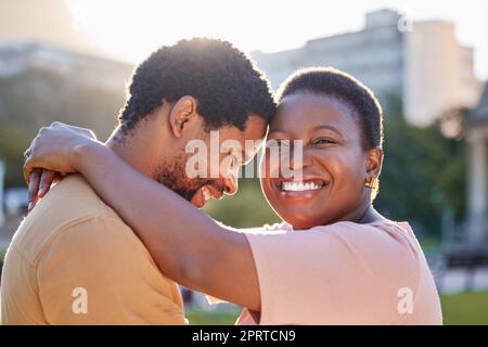 Un couple africain heureux qui s'enserre dans un jardin en plein air pour un pique-nique romantique en été. Sourire, amour et soin entre un homme noir et une femme s'embrassant tout en se tenant debout à l'extérieur. Banque D'Images