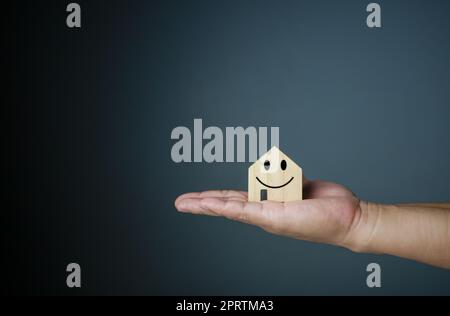 Concept de maison heureuse. Main tenant une maison modèle souriante. Indique le bonheur et l'amour dans la maison. Banque D'Images