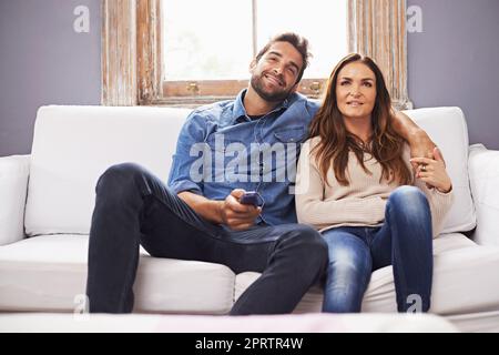 Regarder leurs émissions préférées. Un couple heureux regardant la télévision ensemble sur le canapé à la maison Banque D'Images