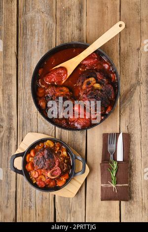 Composition avec l'ossobuco dans une poêle sur une table en bois Banque D'Images