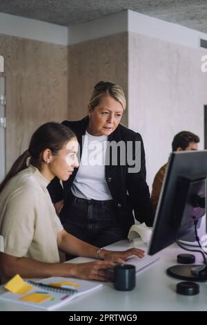 Une professeure explique une étudiante au doctorat sur ordinateur au bureau dans un laboratoire d'innovation Banque D'Images