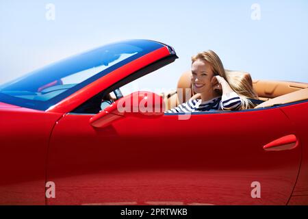 Prêt à mettre quelques kilomètres sur ce bébé. Une jeune femme qui conduit dans une voiture de sport Banque D'Images