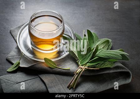 Tasse de thé en sauge et feuilles de sauge sur table grise Banque D'Images