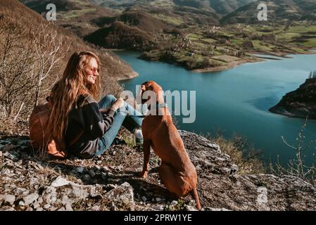 Femme et chien Vizsla assis sur Cliff by River Banque D'Images