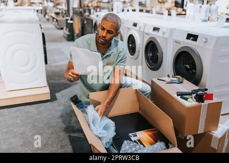 Un vendeur de sexe masculin lit le document lors de l'ouverture de la boîte en carton dans le magasin d'appareils électroménagers Banque D'Images