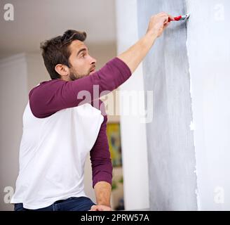 Il veut que ce soit parfait. Photo d'un beau jeune homme peint un mur à l'intérieur. Banque D'Images