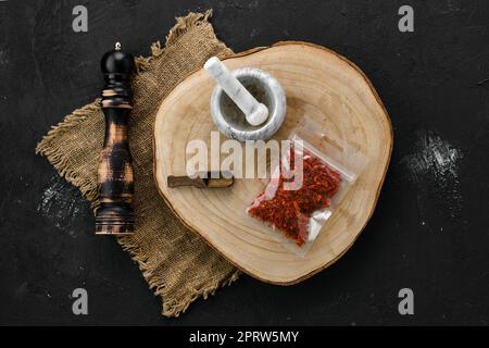 Section transversale en bois avec paprika concassé dans un emballage en plastique et mortier et moulin Banque D'Images