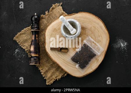 Section en bois avec grains de poivre en emballage plastique et mortier et moulin Banque D'Images