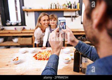 Dites Pizza. Un papa prend une photo de sa famille en train de préparer une pizza maison Banque D'Images