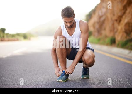 Réglages de dernière minute avant de commencer sa course. Un jeune homme charmant s'est accroupi à l'extérieur tout en ajustant sa chaussure Banque D'Images