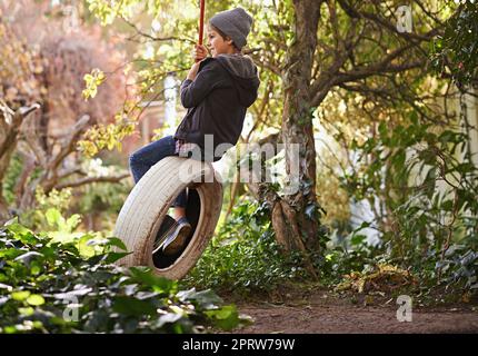 Des journées d'été insouciantes d'une enfance idyllique. Un préadolescent balançant sur une balançoire de pneu dans le jardin. Banque D'Images