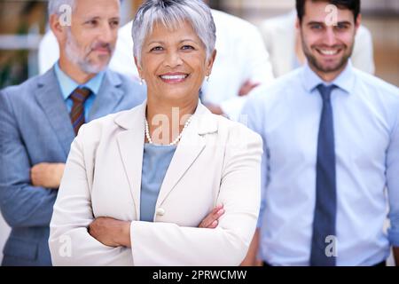 Le succès vient du dur labeur. Portrait d'une femme d'affaires souriante debout devant ses collègues. Banque D'Images