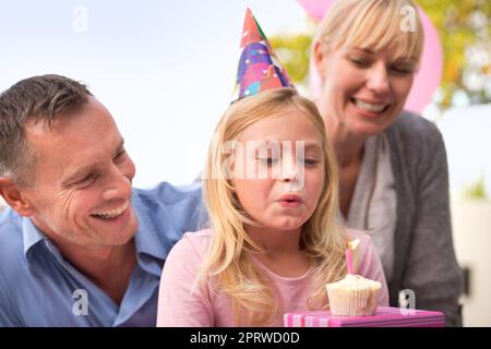 Un souhait pour la fille d'anniversaire. Une photo courte d'une petite fille heureuse et de ses parents célébrant son anniversaire Banque D'Images