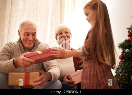 Santas petite aide apporte les cadeaux. Une petite fille donnant à ses grands-parents leurs cadeaux de Noël Banque D'Images