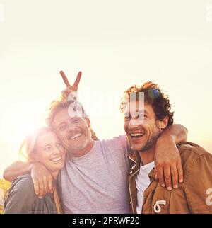 Les amis sont la famille que nous choisissons pour nous-mêmes. Portrait de trois amis debout sur une colline au coucher du soleil. Banque D'Images