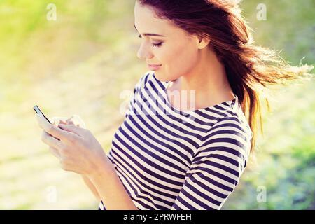 Social dans le soleil. Une jeune femme attrayante utilisant son téléphone mobile à l'extérieur Banque D'Images