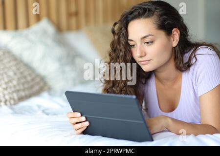 Femme sérieuse utilisant une tablette sur un lit Banque D'Images