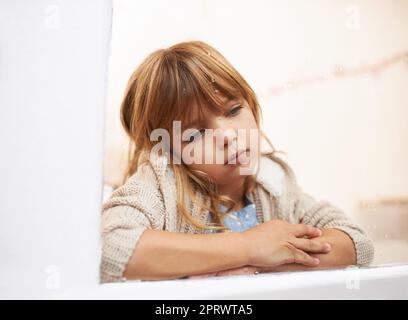 Compter les gouttes de pluie. Une petite fille lasse assis et regardant par une fenêtre un jour pluvieux Banque D'Images