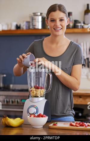 Baies de bons ingrédients en effet. Portrait d'une jeune femme attrayante ajoutant des fruits frais à un mélangeur pour faire un smoothie Banque D'Images