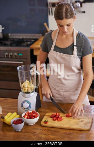 Préparer des smoothies frais et fruités. Une jeune femme hache des fruits pour faire un smoothie Banque D'Images