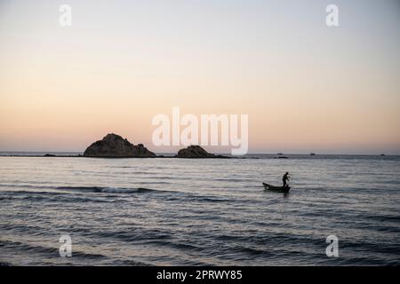 Silhouette d'un pêcheur se préparant à jeter les filets dans la mer au coucher du soleil. Banque D'Images