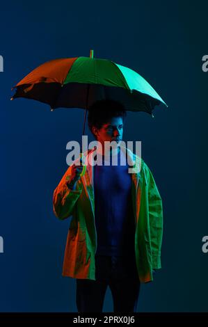 Homme en imperméable sous parapluie sur fond sombre de studio Banque D'Images