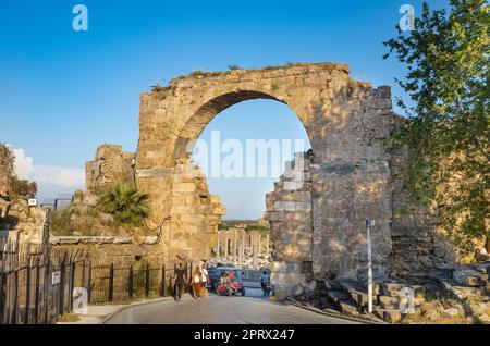 Les touristes se promènent à travers la porte Monumental près du monument Vespasien tandis qu'un buggy électrique se déplace l'autre côté de l'ancienne ville romaine en Turquie (T Banque D'Images