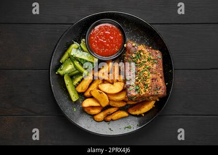 Vue en hauteur des côtes de bœuf rôties avec des quartiers de pommes de terre et du concombre mariné Banque D'Images