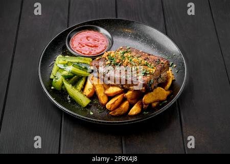 Côtes de bœuf rôties avec des quartiers de pommes de terre et du concombre mariné Banque D'Images