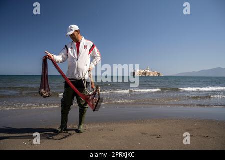 Homme collectant des coquillages sur la plage de Tayeth en face du Rocher d'Al Hoceima. L'île est le territoire espagnol au large de la côte du Maroc Banque D'Images