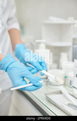Gros plan de la brosse blanche avec crème visage de luxe dans les mains d'esthéticienne. Produits de soins pour la peau Banque D'Images