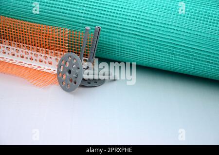 Un ensemble d'éléments de construction pour l'isolation des murs. Chevilles en plastique, un rouleau de grillage pour l'isolation des façades et un profil d'angle avec une grille Banque D'Images