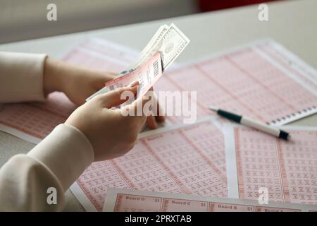 Une jeune femme tient le billet de loterie avec une rangée complète de nombres et de billets de dollars sur le fond de feuilles vierges de loterie. Concept gagnant de loterie Banque D'Images