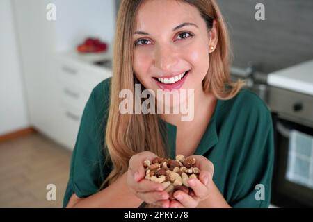 Femme souriante en bonne santé montrant un mélange de fruits secs aux noix dans ses mains à l'appareil photo Banque D'Images