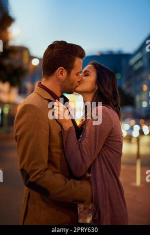 Tomber fou, profondément et vraiment dans l'amour. un jeune couple affectueux partage un baiser dehors la nuit Banque D'Images