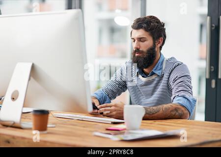 Nous allons nous réunir pour déjeuner pour discuter plus avant du projet. un jeune texte créatif sur un téléphone portable tout en étant assis à un ordinateur dans un bureau Banque D'Images