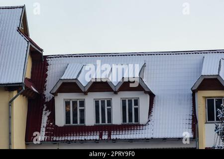 Neige sur le toit d'un toit métallique rouge et marron d'une maison européenne avec une fenêtre. Banque D'Images