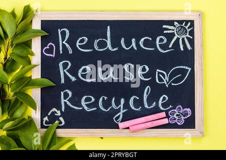 Tableau à craie affiche de recyclage Reuse sur fond jaune avec feuilles vertes et craies. Vue de dessus Banque D'Images
