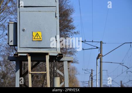 Transformateur électrique en gris avec un symbole d'avertissement du danger de tension élevée près de la ligne de chemin de fer. Un petit poste pour la fourniture d'electri Banque D'Images