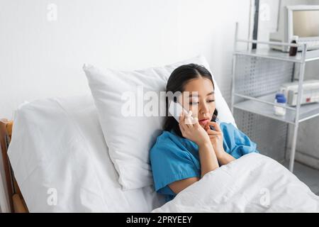 contrarié femme asiatique tenant la main près du visage tout en parlant sur téléphone mobile dans le service de l'hôpital, image de stock Banque D'Images