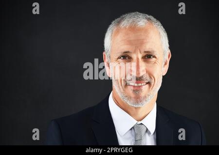 Je prends soin de l'entreprise. Portrait studio d'un homme d'affaires mûr souriant sur fond noir Banque D'Images