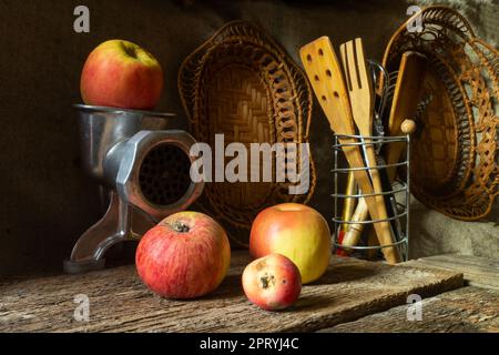 Pommes mûres avec ustensiles de cuisine. Fruit avec un moulin à viande sur une table en bois ancienne Banque D'Images