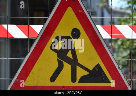 Le panneau d'avertissement 'en construction' est attaché à une clôture en treillis métallique avec un rouge et blanc rayé de bandes de signal Banque D'Images