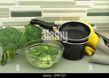 Bouquets de brocoli frais trempés dans un bol d'eau claire à côté de la poêle et du pot. Concept frit ou bouilli Banque D'Images