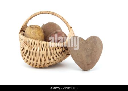 Pomme de terre en forme de coeur à côté d'un panier en osier avec des pommes de terre de différents types et couleurs isolées sur fond blanc Banque D'Images