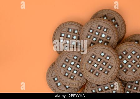 Image détaillée du marron foncé sandwich cookies ronde avec remplissage de coco sur une surface orange. Image d'arrière-plan d'un close-up de plusieurs gâteries pour Banque D'Images